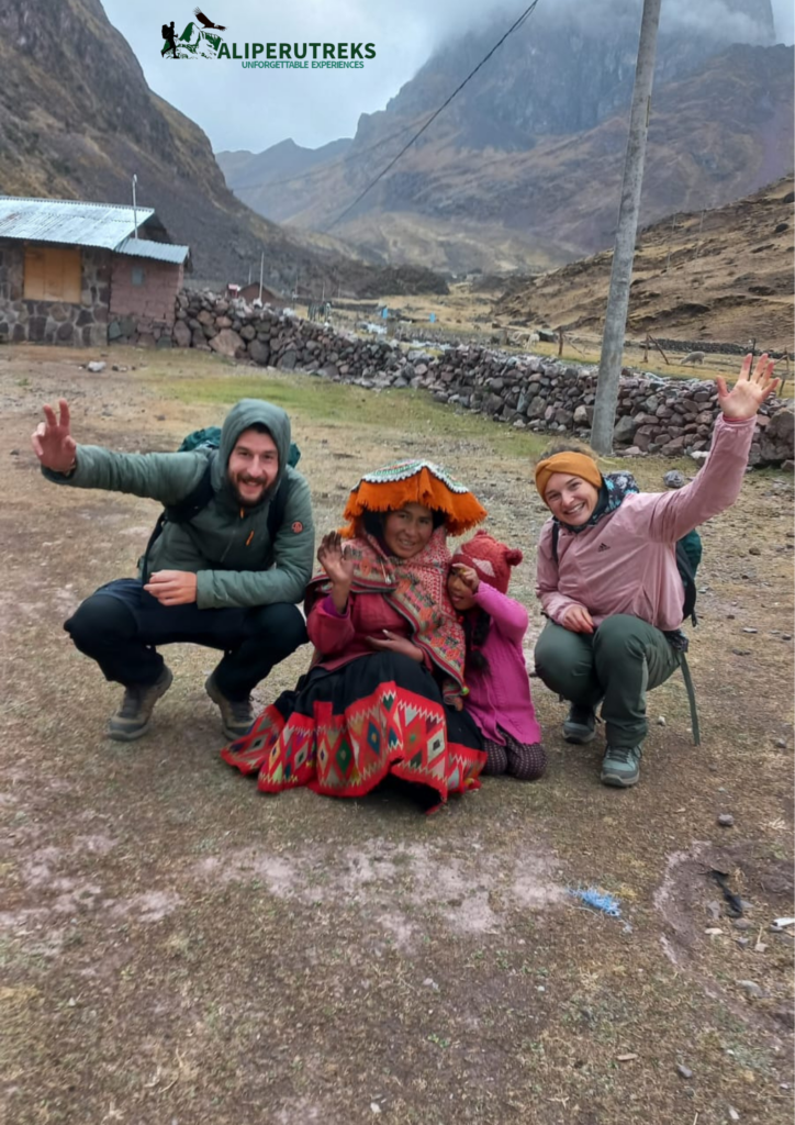 Two smiling trekkers pose with a local Andean woman and child, who are wearing colorful traditional clothing, showcasing authentic Andean Cultural Immersion during a guided trek. - Ali Peru Treks