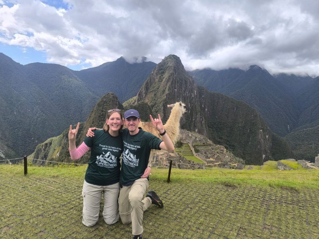 Happy couple posing with a llama overlooking the ruins on Machu Picchu tours - Ali Peru Treks