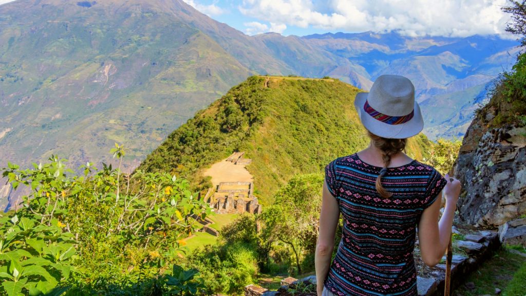 A traveler with a hat and a walking stick admires the breathtaking view, an ancient Inca site nestled in the lush mountains of Peru – Ali Peru Treks