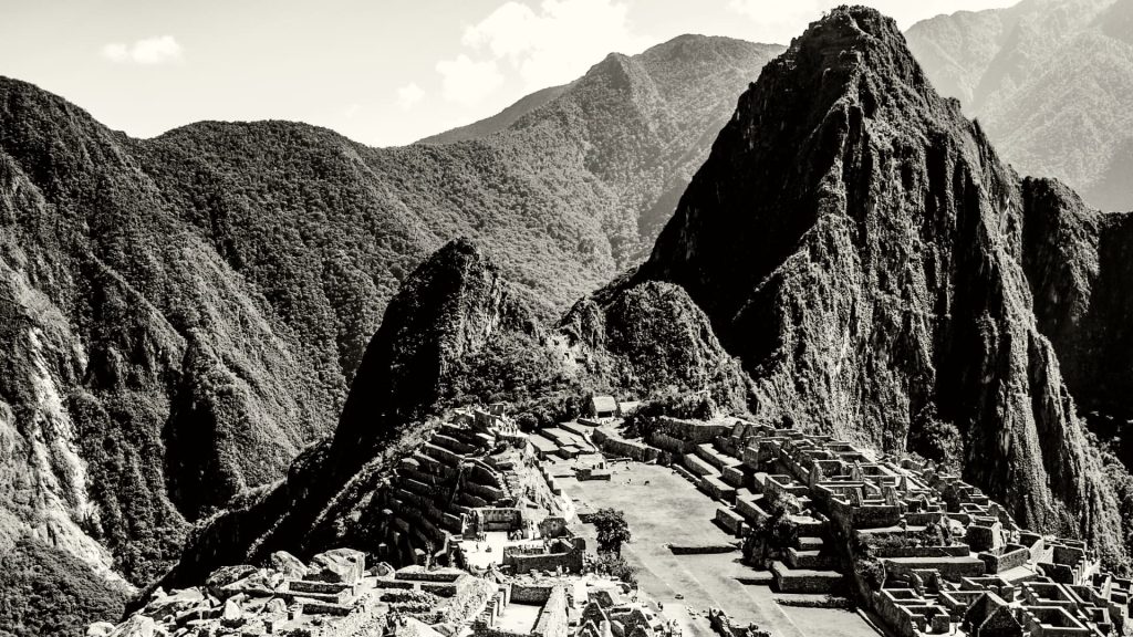 Black and white image of Machu Picchu, showcasing the ancient Inca ruins surrounded by lush mountains, highlighting the enduring legacy of Inca Culture - Ali Peru Treks.