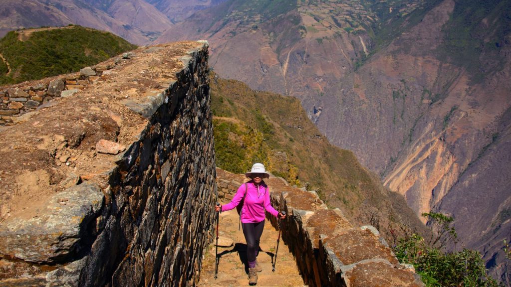 A female trekker in a pink jacket hiking along the ancient Inca stone pathways of Choquequirao, surrounded by breathtaking mountain views – Ali Peru Treks