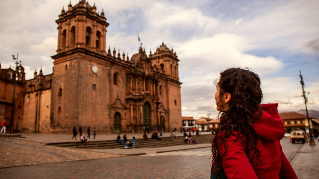 A traveler in a red jacket admires the Cusco Cathedral in the Plaza de Armas, capturing the charm and history of this iconic landmark in Peru. - Ali Peru Trek.
