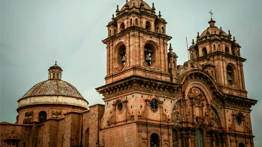 A close-up view of a historic colonial church in Cusco, Peru, highlighting its intricate architecture and towering bell towers against a cloudy sky.