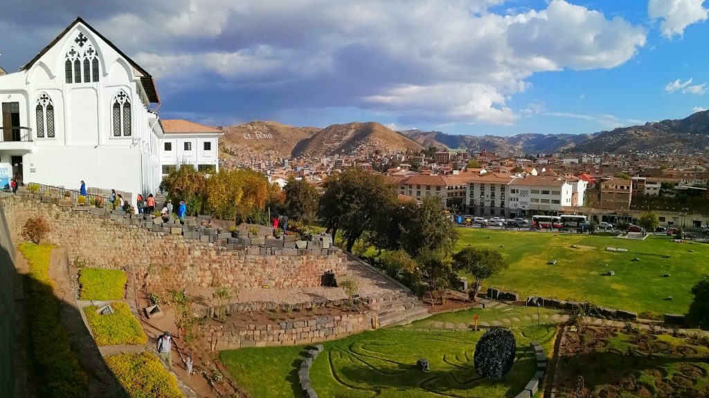 A breathtaking view of the Qorikancha Gardens in Cusco, Peru, featuring ancient Inca stone walls, colonial architecture, and the scenic Andean mountains. - Ali Peru Trek.