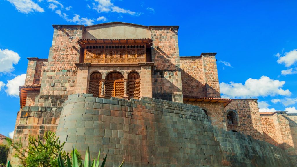 The stunning facade of Qorikancha in Cusco, Peru, showcasing the fusion of Inca stonework and colonial Spanish architecture under a bright blue sky. - Ali Peru Trek.