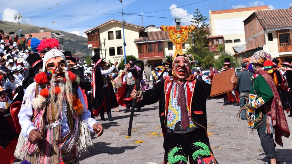 Traditional Andean dancers in embroidered costumes and masks performing in a cobblestone plaza, possibly part of Cruz Velacuy festivities – Ali Peru Treks