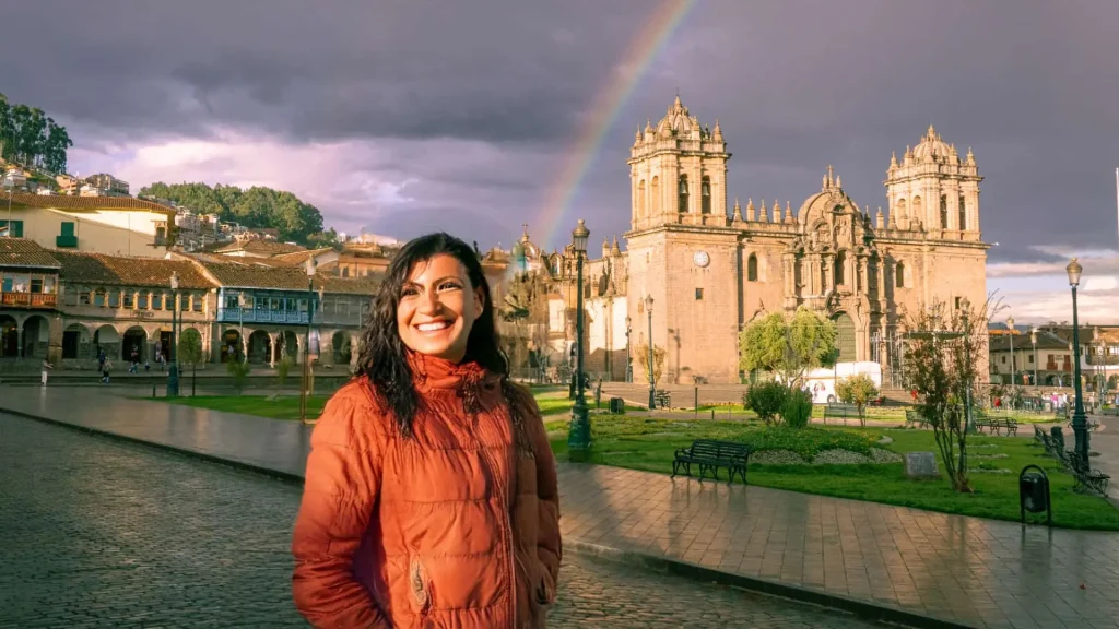 Smiling traveler with rainbow in front of Cuscos cathedral